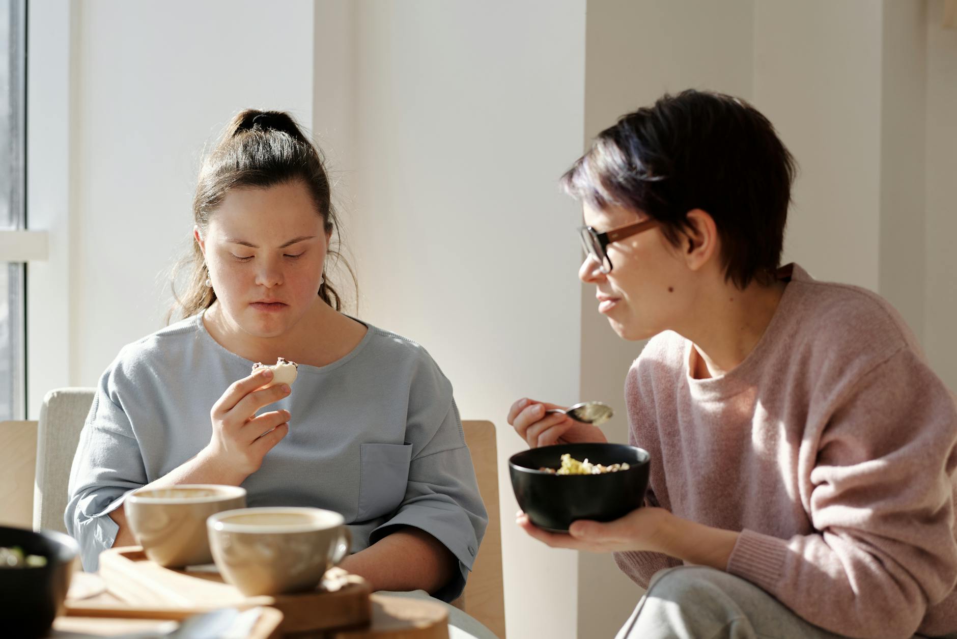 Two women sharing breakfast together in a supported living home, one with Down syndrome, fostering togetherness and daily independence